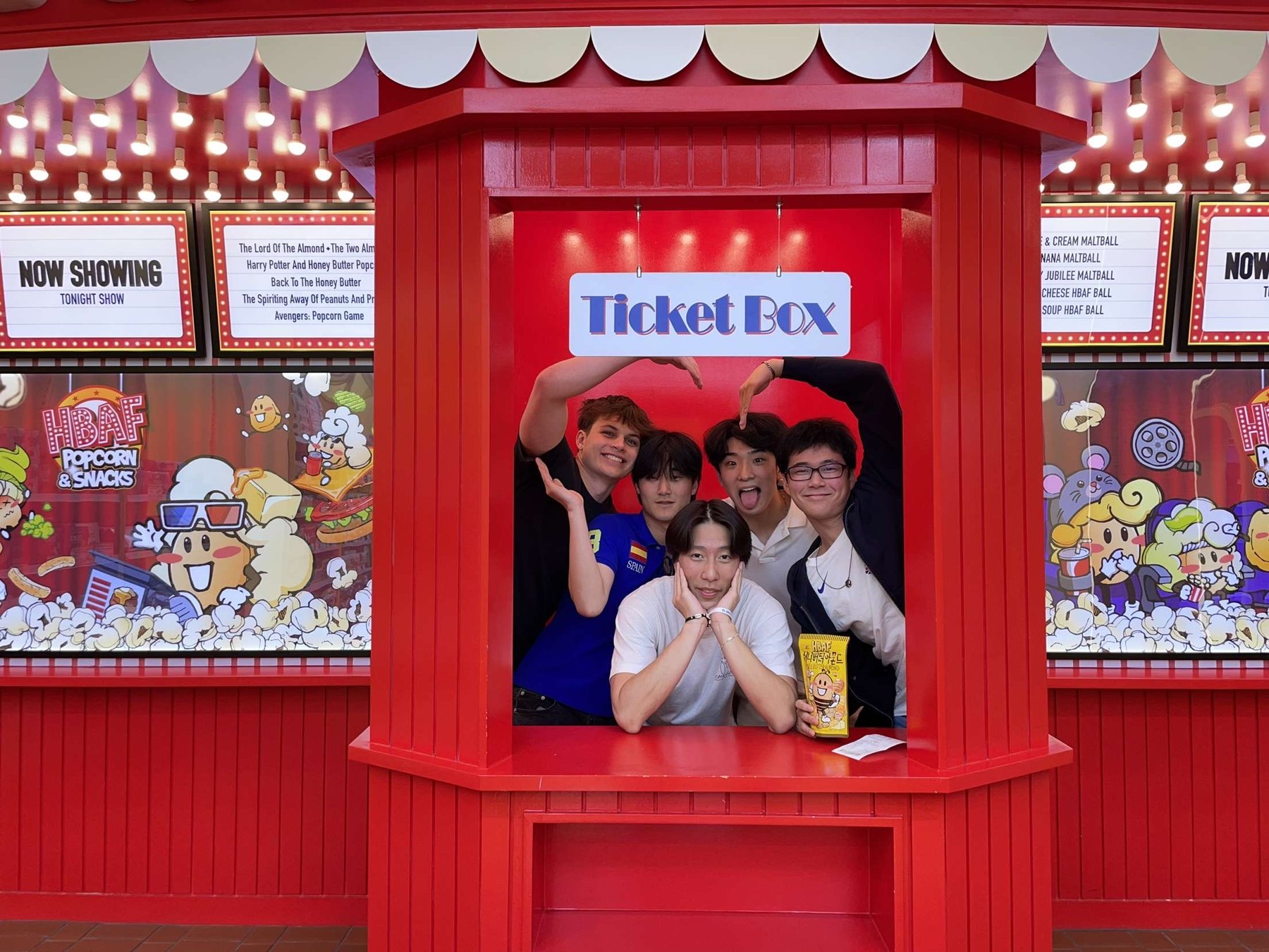 Friends posing together inside a bright red ticket booth.